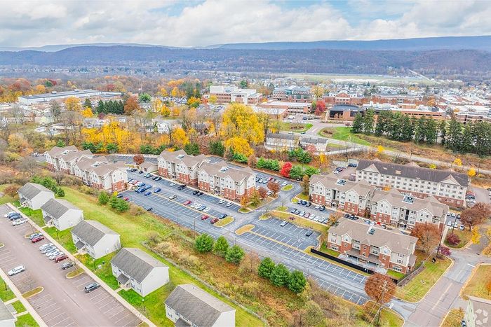 Scenic aerial view of picturesque apartment complex nestled in vibrant autumn landscape, featuring well-maintained buildings and spacious parking area.