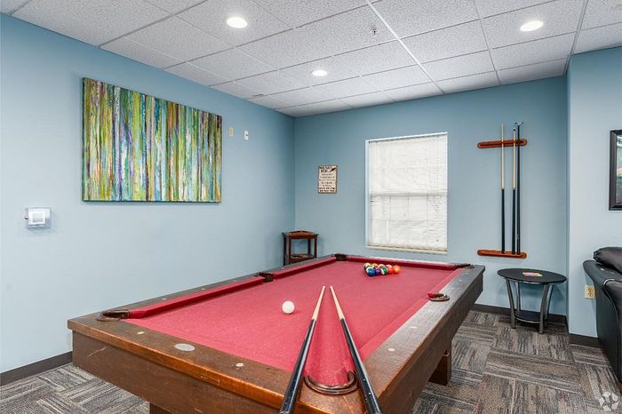 Modern apartment recreation room with vibrant artwork and a sleek red-felted pool table for entertainment.