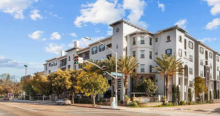 Elegant multi-story apartment complex with classic architecture and palm-lined streets under a sunny sky, showcasing modern urban living.