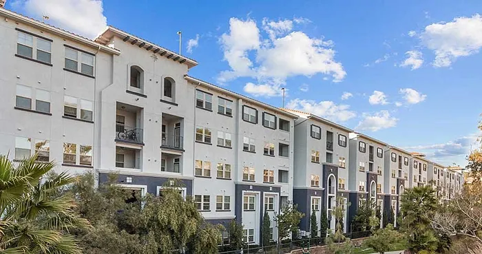 Charming multi-story apartment building with elegant architecture, framed by lush greenery and a bright blue sky.