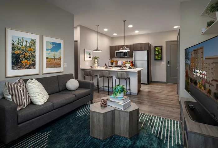 Modern living area with stylish decor, cozy gray sofa, vibrant wall art, and sleek kitchen featuring stainless steel appliances and a chic breakfast bar.