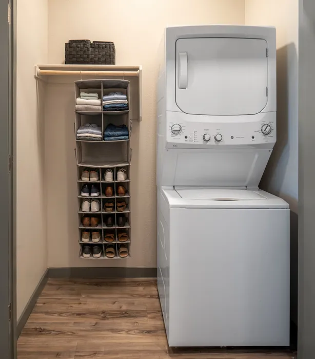 Efficient laundry room with a modern stacked washer and dryer, ample shelving, and stylish shoe organizer.