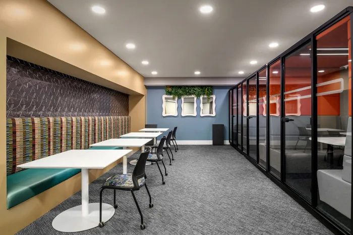 Modern coworking space with colorful seating, white tables, and glass partitioned meeting rooms, creating an inviting and collaborative environment.