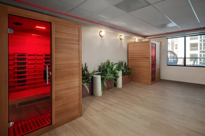 Elegant wellness room featuring a modern infrared sauna, stylish wood panels, and vibrant green plants under soft lighting.