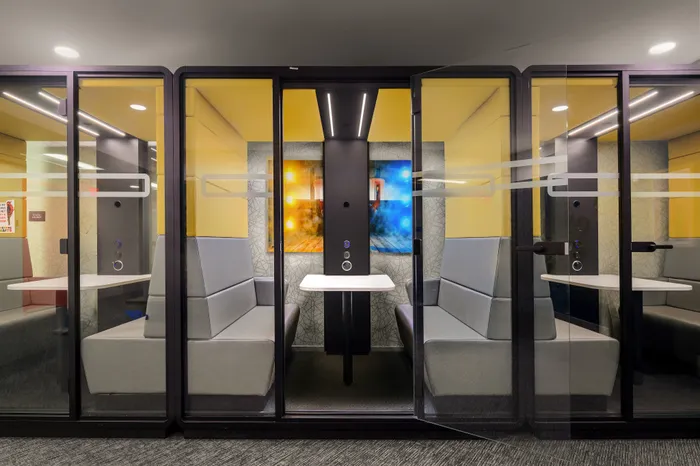 Modern office meeting pod with sleek glass doors, comfortable seating, and vibrant wall art.