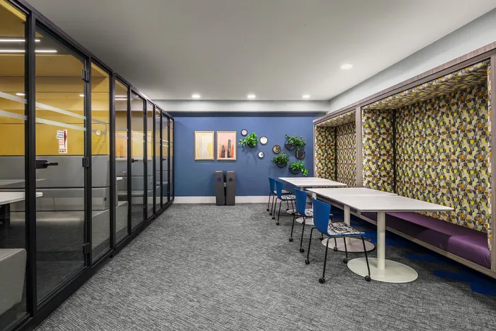 Modern co-working space with colorful wall art, sleek partitioned offices, and vibrant communal seating area.