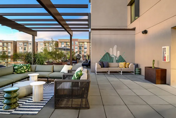 Chic outdoor patio with stylish seating, vibrant cushions, and modern pergola, overlooking urban apartments.