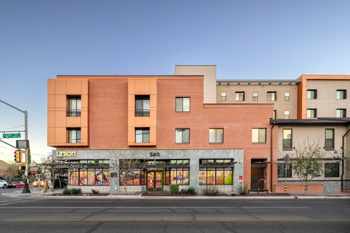 Modern urban apartment building with striking brick facade and vibrant mural, located at a bustling city corner.