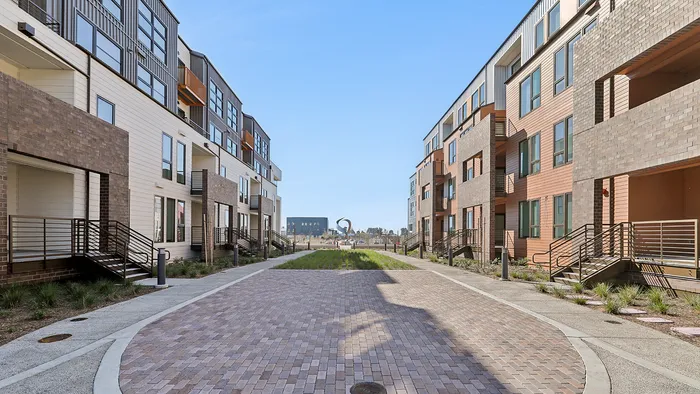 Modern urban apartment complex with stylish facades and spacious walkways under a clear blue sky.