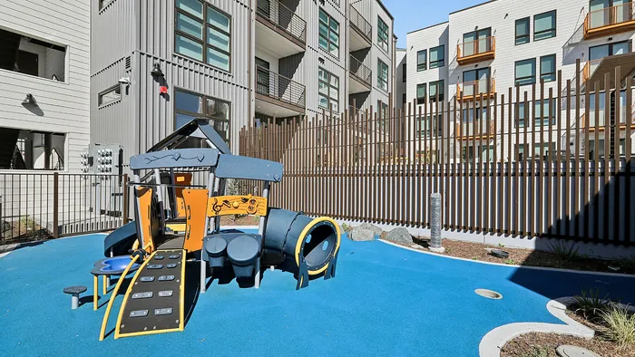 Modern apartment building with a vibrant playground set on a bright blue surface, ideal for family-friendly living.