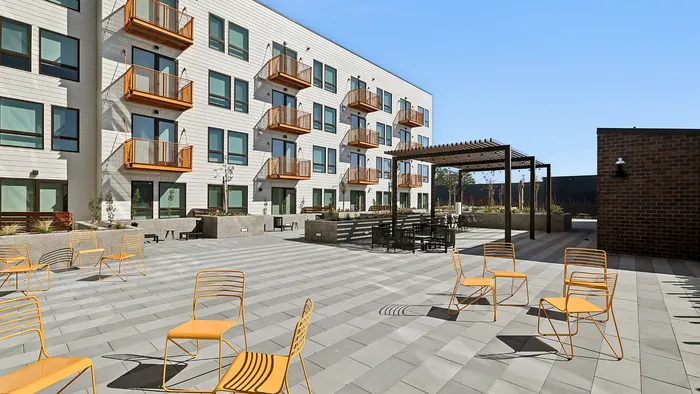 Modern apartment building with stylish balconies and a vibrant outdoor patio featuring bold orange chairs and seating area under a sleek pergola.