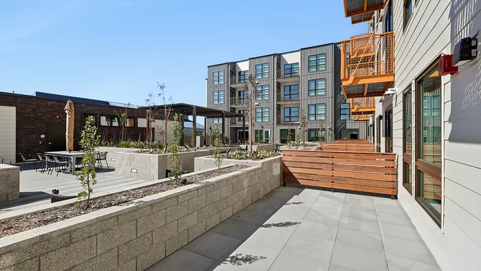 Modern apartment exterior with stylish balconies, landscaped communal area, and inviting outdoor seating.