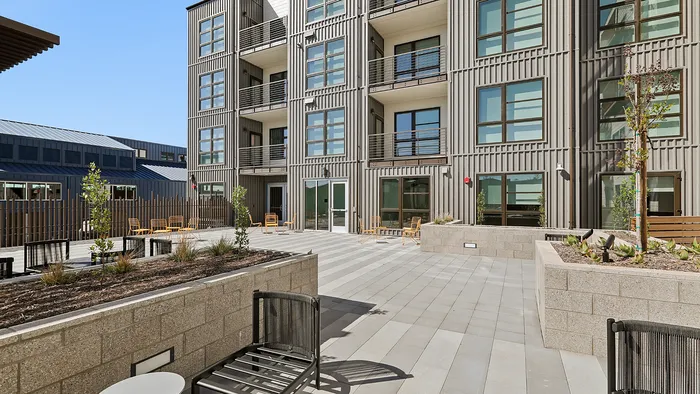 Modern apartment exterior with stylish balconies and spacious courtyard featuring seating and landscaped planters.