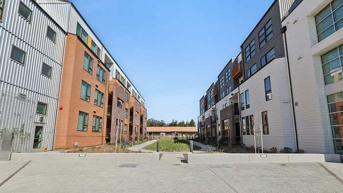 Chic urban apartment complex with modern architecture, featuring wide walkways and a landscaped central courtyard under a clear blue sky.