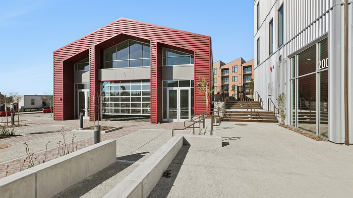 Modern architectural exterior featuring a striking red facade with large glass windows, surrounded by a spacious and inviting outdoor area.