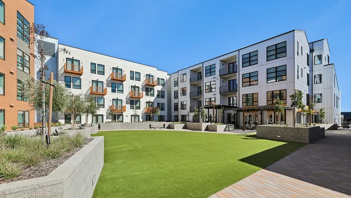 Modern apartment complex exterior with stylish balconies, lush green courtyard, and vibrant architectural design.