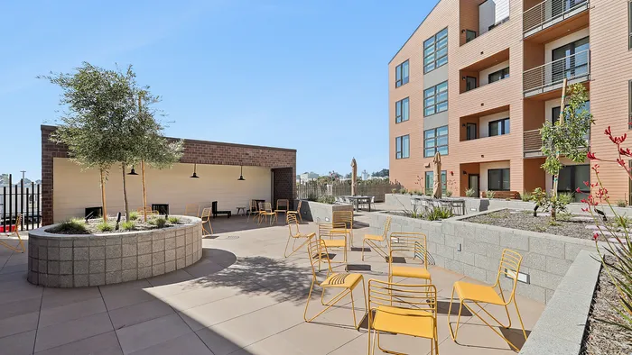 Modern apartment courtyard featuring stylish yellow outdoor seating, lush planters, and contemporary building architecture.