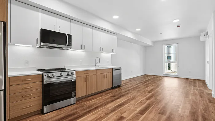 Bright, modern kitchen with sleek cabinetry, stainless steel appliances, and open living space with large window and elegant wood flooring.