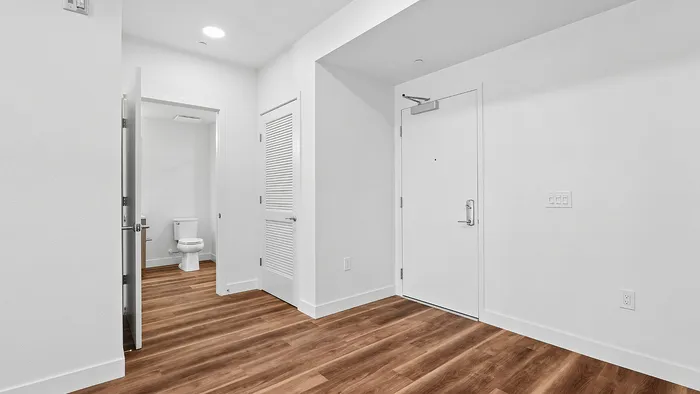 Modern apartment entryway with elegant hardwood floors leading to a bright, pristine bathroom.