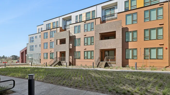 Modern apartment building exterior with a blend of wood and brick facade, featuring large windows and inviting balconies, surrounded by peaceful greenery.