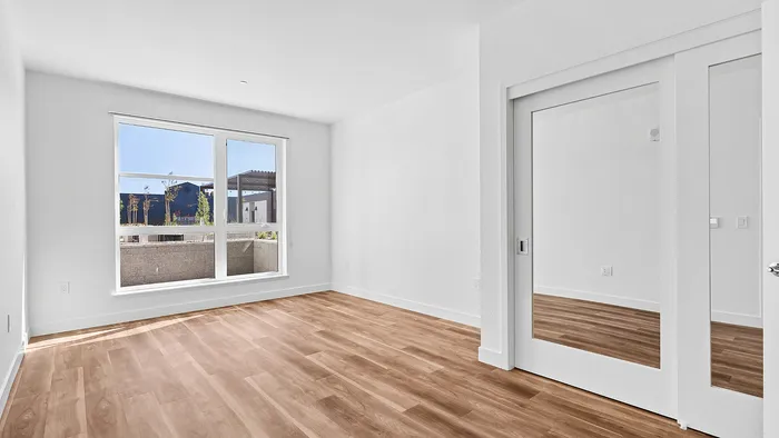 Bright and airy bedroom featuring sleek hardwood floors, a large window with picturesque views, and modern mirrored closet doors.