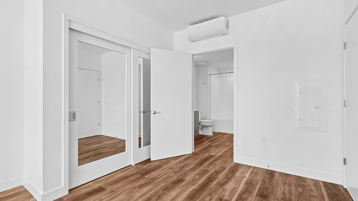 Bright and modern room featuring elegant wooden flooring, a large mirrored closet, and an en-suite bathroom.