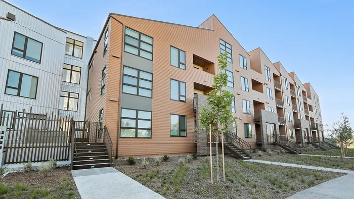 Modern multi-story apartment building with sleek design, large windows, and neatly landscaped surroundings.