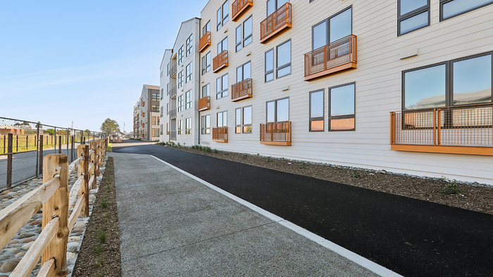 Modern apartment facade with multiple windows and orange balconies overlooking a scenic walkway, exuding urban charm and convenience.