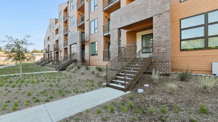 Modern apartment complex with attractive brick and wood facade, featuring multiple balconies and lush landscaped surroundings.