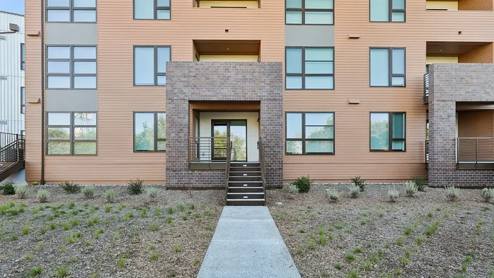 Modern apartment exterior with stylish brick accents and large windows, highlighted by a welcoming entrance and landscaped greenery.