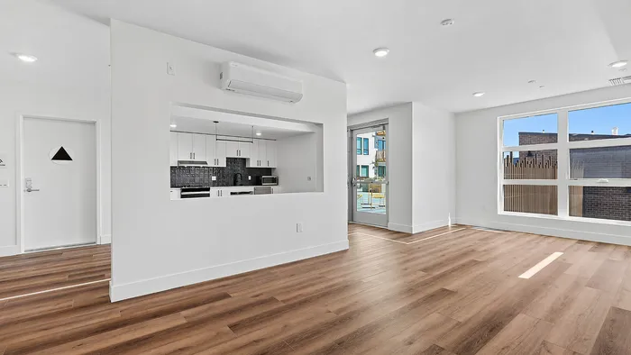 Modern open-concept apartment with hardwood floors, a sleek kitchen view, and abundant natural light from large windows.