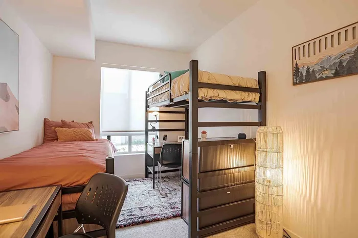 Bright and cozy bedroom with stylish loft bed, modern desk setup, and large window offering natural light, perfect for student living.