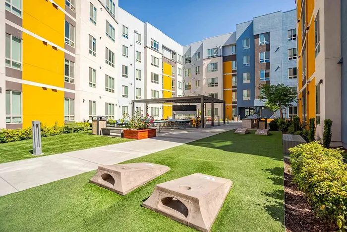 Vibrant apartment courtyard featuring modern architecture, lush greenery, and a stylish outdoor seating area with games.
