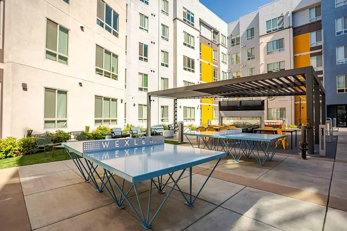 Modern apartment courtyard with stylish ping pong tables and outdoor seating under a sleek pergola, perfect for relaxation and social gatherings.