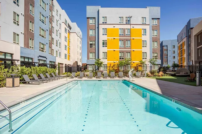 Vibrant apartment complex showcasing modern architecture with a large, inviting outdoor pool and sun loungers, perfect for relaxation.