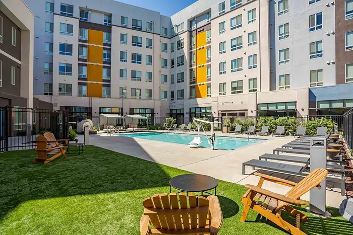 Contemporary apartment complex courtyard featuring a pristine pool, ample lounging areas, and modern architectural design.