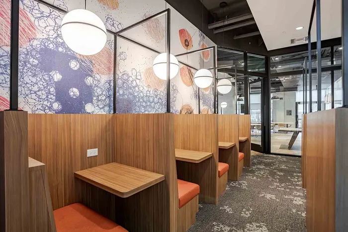 Modern workspace with sleek wooden booths, vibrant seating, artistic wall design, and stylish lighting.