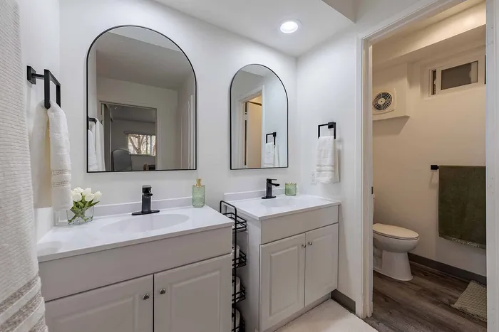 Elegant bathroom featuring dual sinks with sleek black fixtures, stylish arched mirrors, and contemporary decor accents.