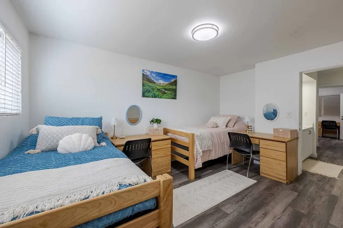 Bright and inviting shared bedroom with cozy twin beds, modern decor, and ample natural light, perfect for a comfortable living experience.