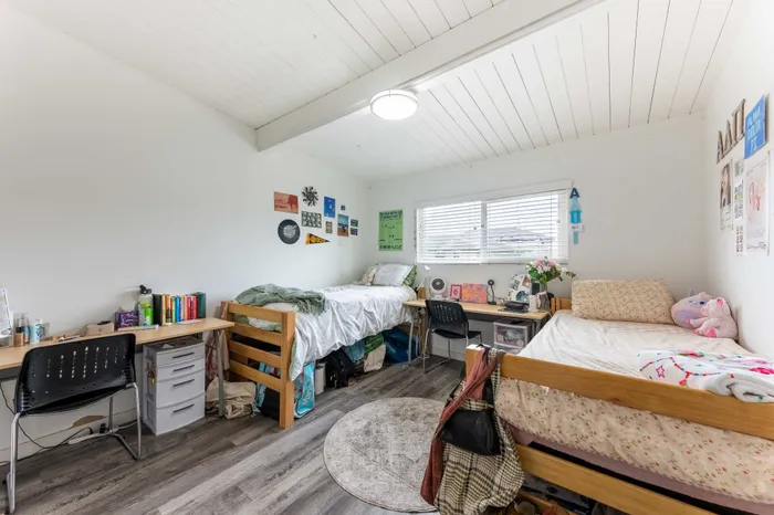 Bright and inviting dual-bedroom space with stylish decor, featuring cozy beds, functional desks, and decorative wall accents.