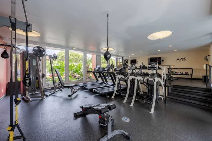 Bright and modern fitness center equipped with treadmills, weight machines, punching bag, and a set of dumbbells, offering a motivating workout space with large windows and inspiring decor.