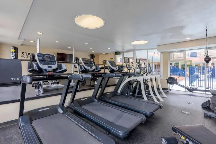 Bright and modern fitness center with state-of-the-art treadmills, exercise bikes, and weight training equipment, offering a vibrant workout environment with poolside views.