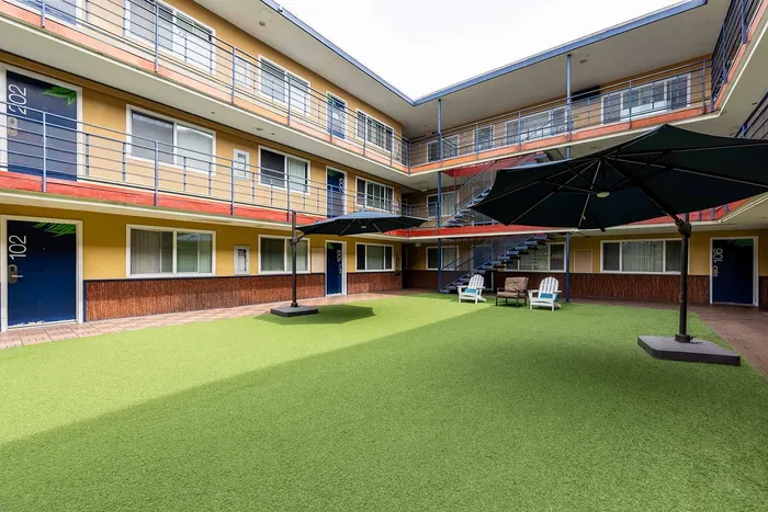 Charming apartment complex with vibrant exterior, featuring a lush green courtyard with stylish seating and large umbrellas.