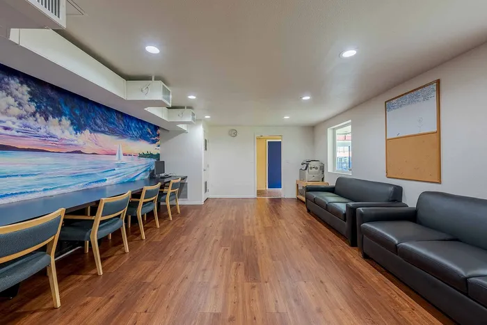 Inviting communal workspace with vibrant ocean mural, featuring sleek wooden flooring and comfortable seating.