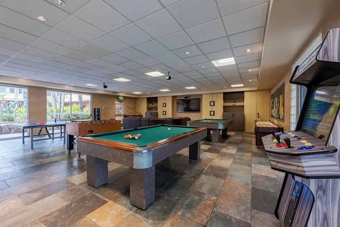 Elegant recreation room featuring billiards tables, a foosball table, and an arcade machine in a well-lit, modern space.