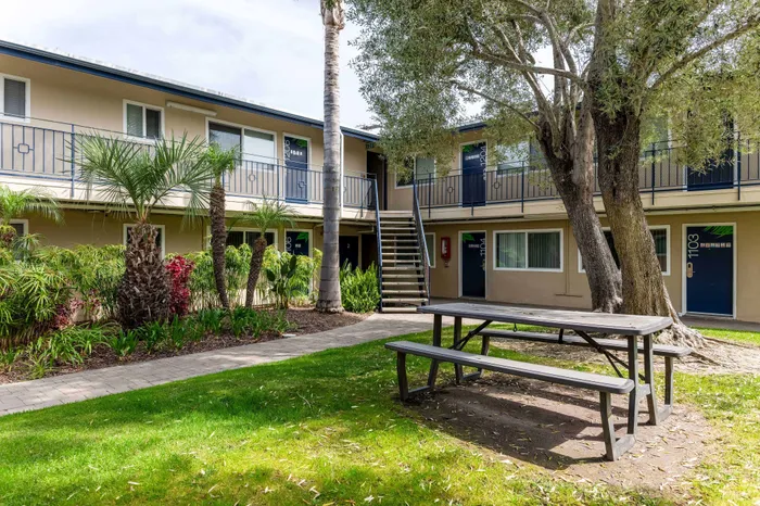 Charming apartment complex with lush landscaping, featuring outdoor seating and surrounded by vibrant greenery.