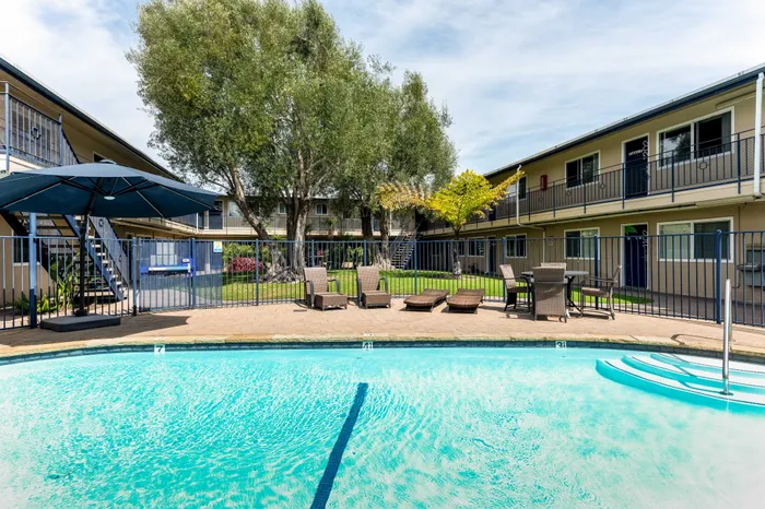 Bright apartment complex with lush greenery and a sparkling outdoor pool, perfect for relaxation and leisure.