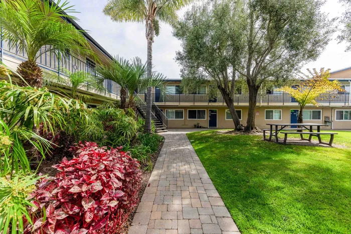 Charming apartment courtyard with lush tropical landscaping, palm trees, and a welcoming picnic area.