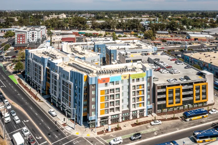 Aerial view of a modern, vibrant apartment complex with colorful facades and ample parking in a bustling urban area.