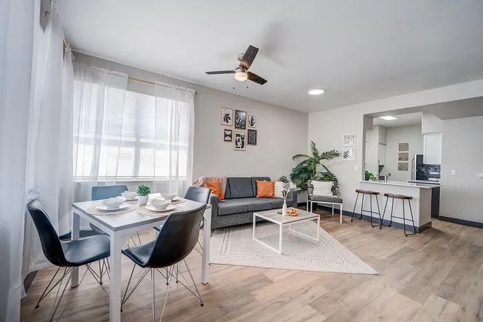Bright and airy living space featuring a modern open-plan design with cozy seating area, stylish dining table, and sleek kitchen bar with stools.